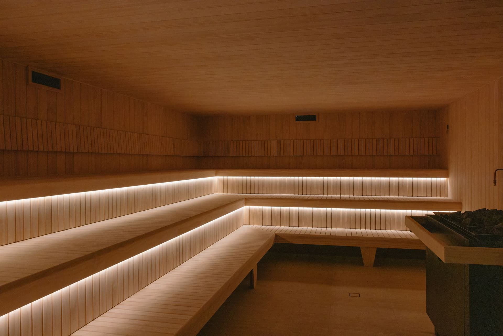 Empty Finnish sauna interior with long tiered benches lit from below and a stone-filled heater at right
