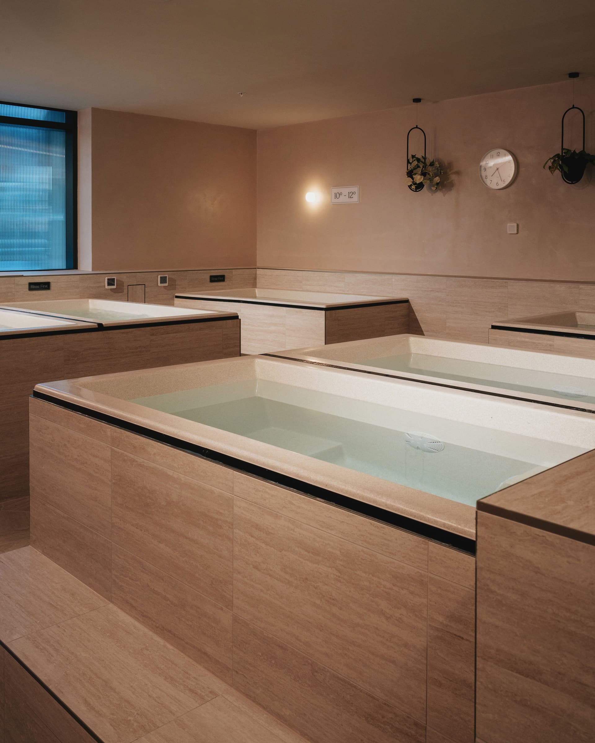Stone-clad cold plunge baths filled with still water, with a wall clock and a temperature plaque above