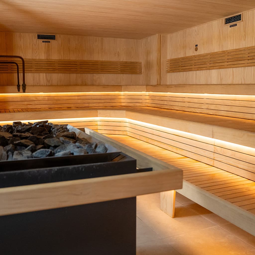 An empty Finnish sauna, its black stove filled with stones in front of tiered timber benches