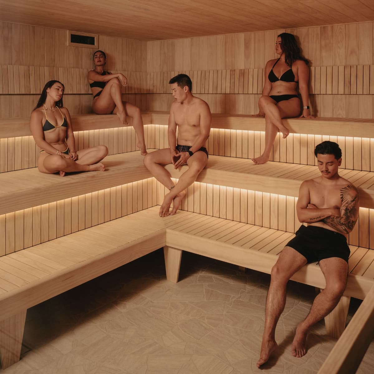 Six people sitting on the tiered timber benches of a large Finnish sauna