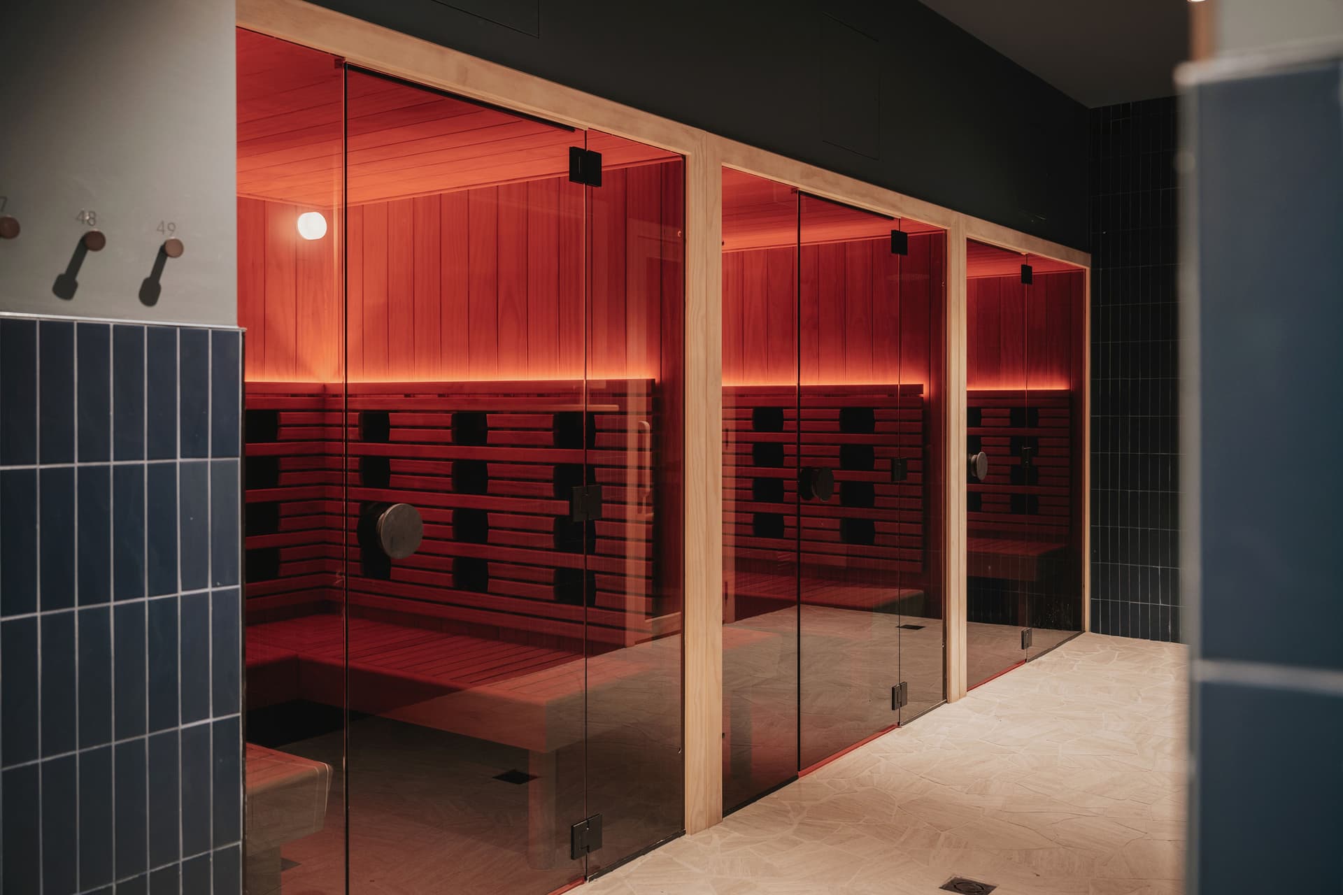 Three glass-fronted infrared sauna cabins glowing red beside a wall of dark blue tiles