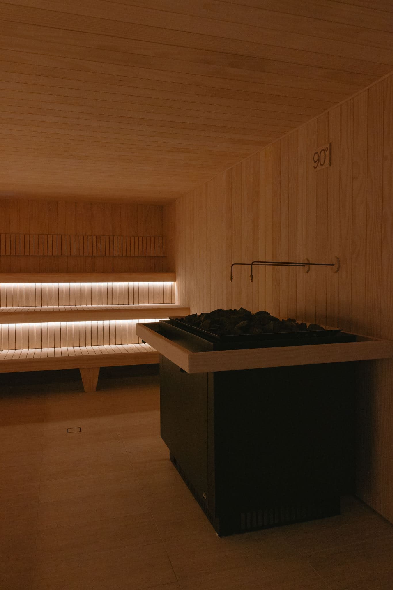 Empty Finnish sauna interior with long tiered benches lit from below and a stone-filled heater at right