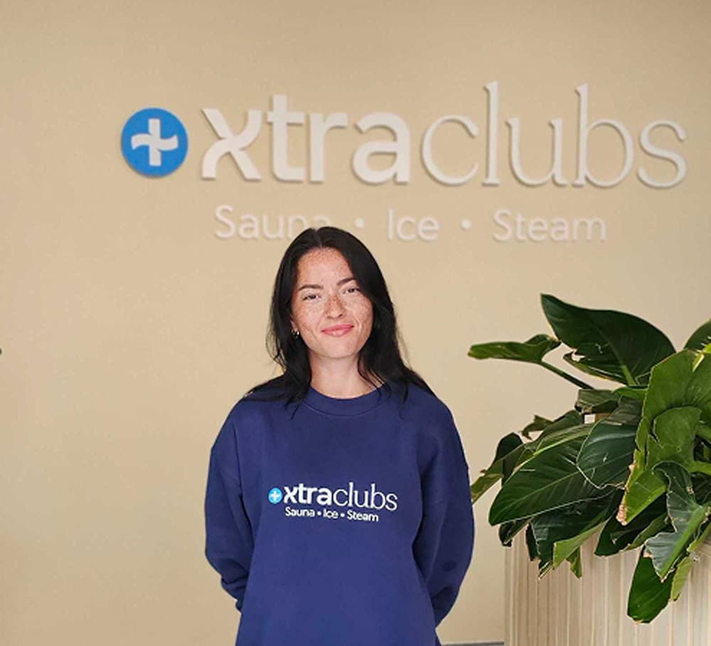A team member in an XtraClubs sweatshirt standing under the sign in reception