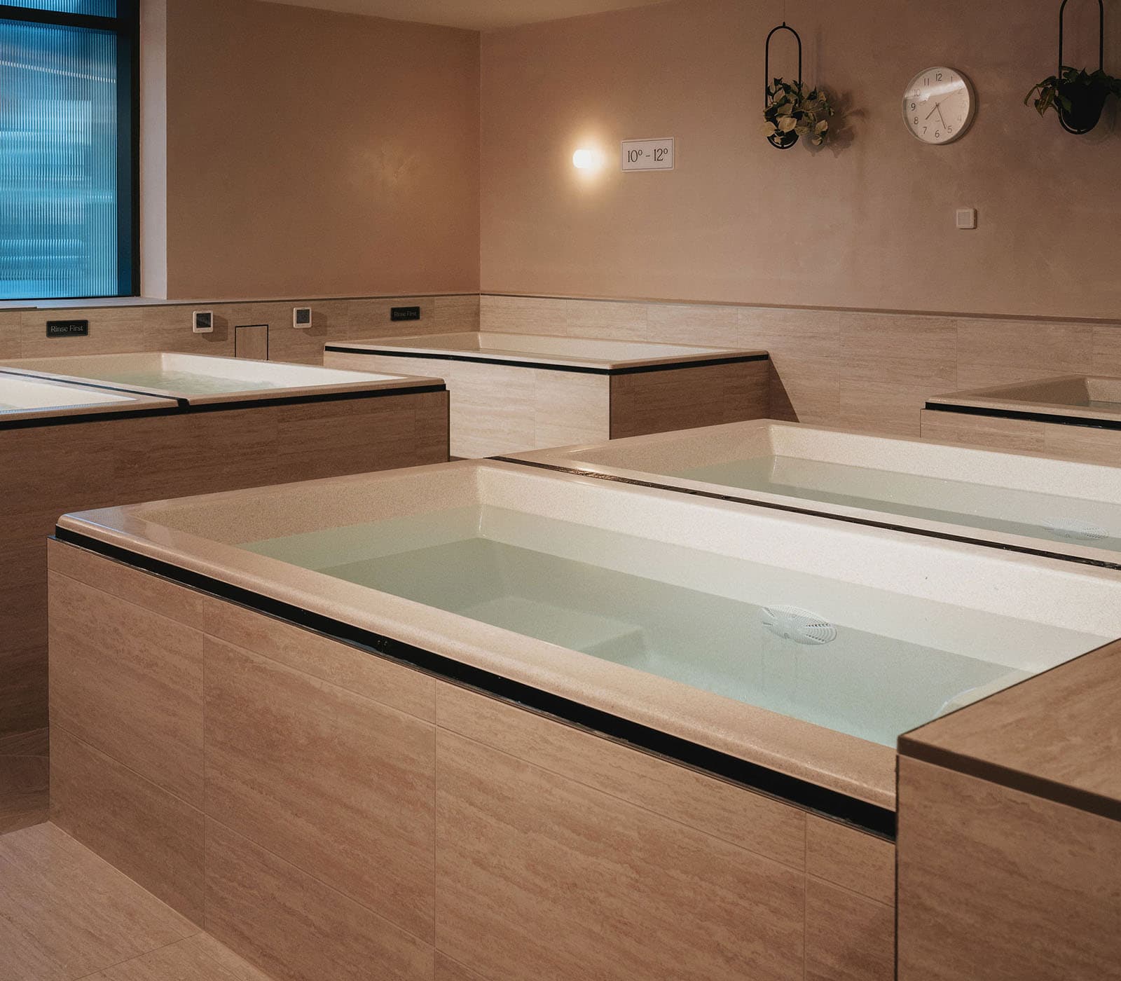 Four timber-clad ice baths in a room with a wall clock and hanging plants