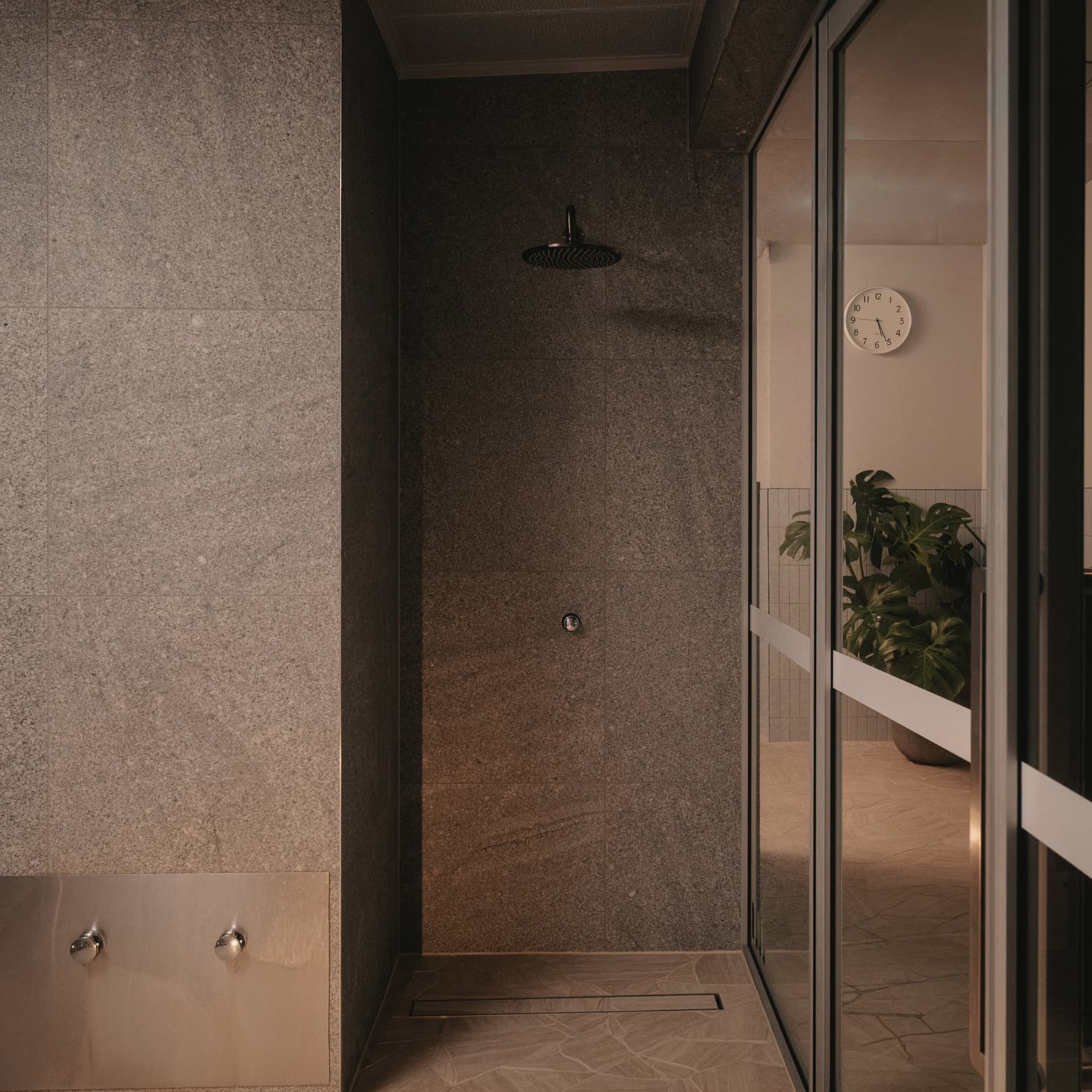 A stone-tiled shower alcove with a rain head, beside a glass door