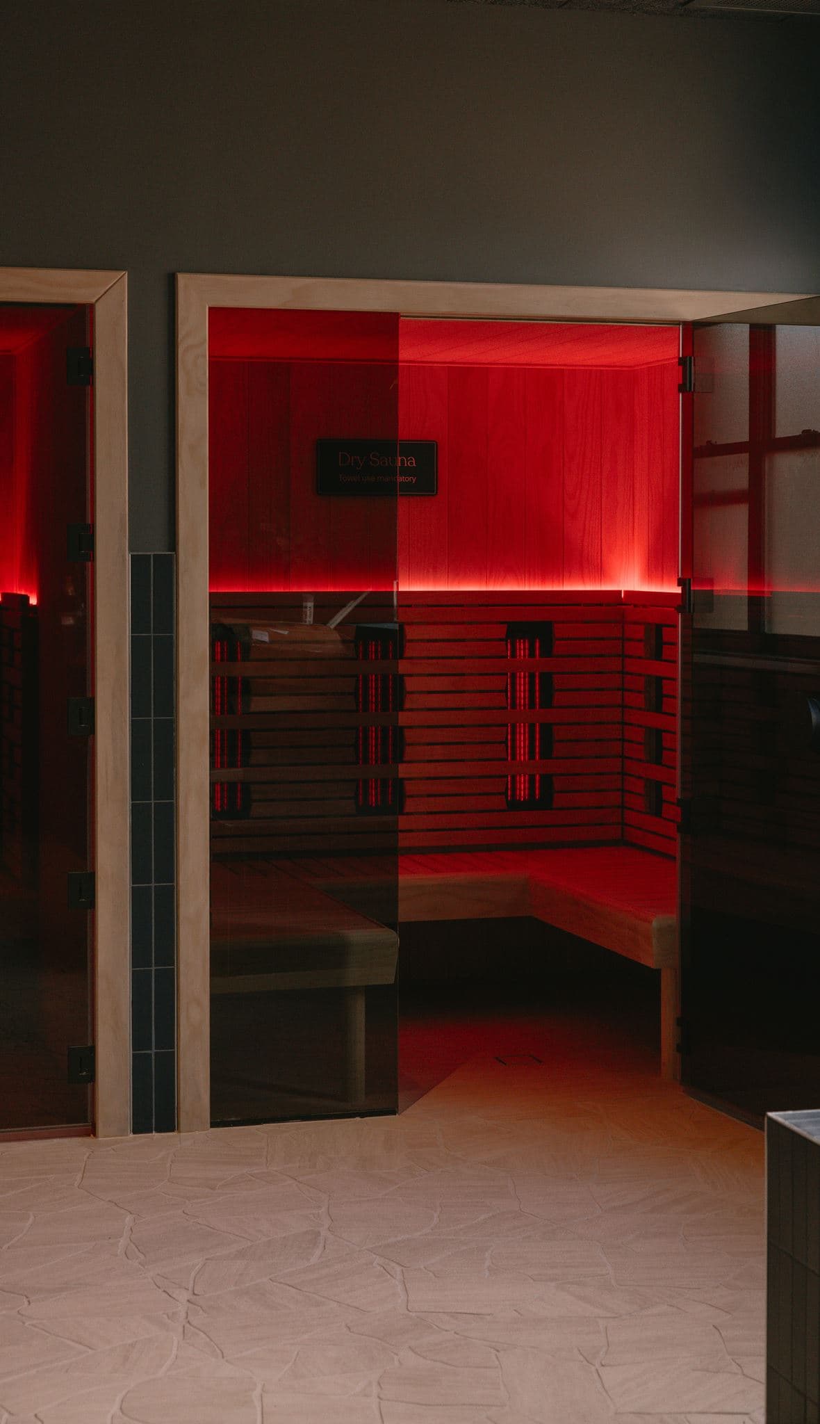 Glass-fronted dry sauna cabin glowing red, its infrared panels set behind slatted timber benches
