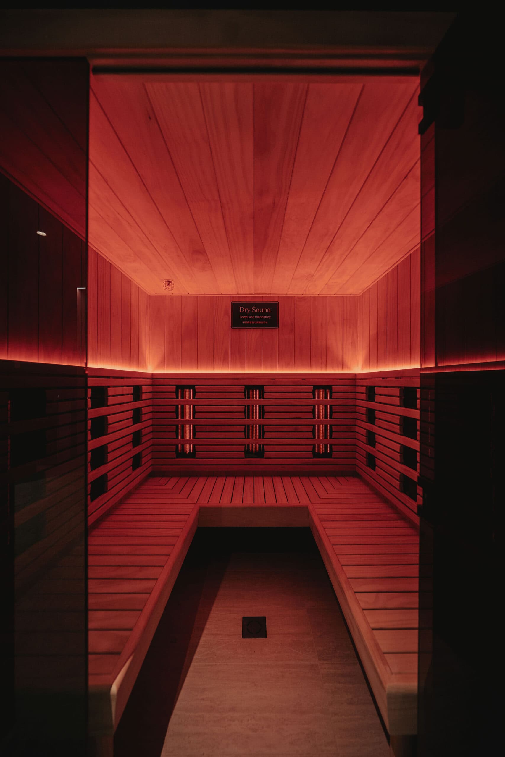 An empty infrared sauna seen from the doorway, its heating panels glowing red along both side walls