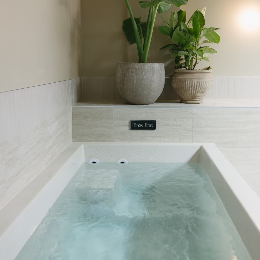 A cold plunge pool of pale still water, potted plants on the ledge above
